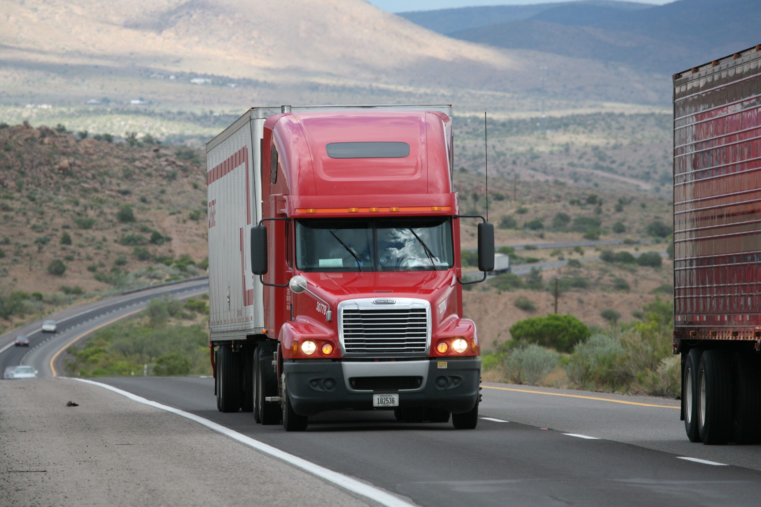 project-1 Red semi-truck driving through scenic highway in a mountainous landscape.