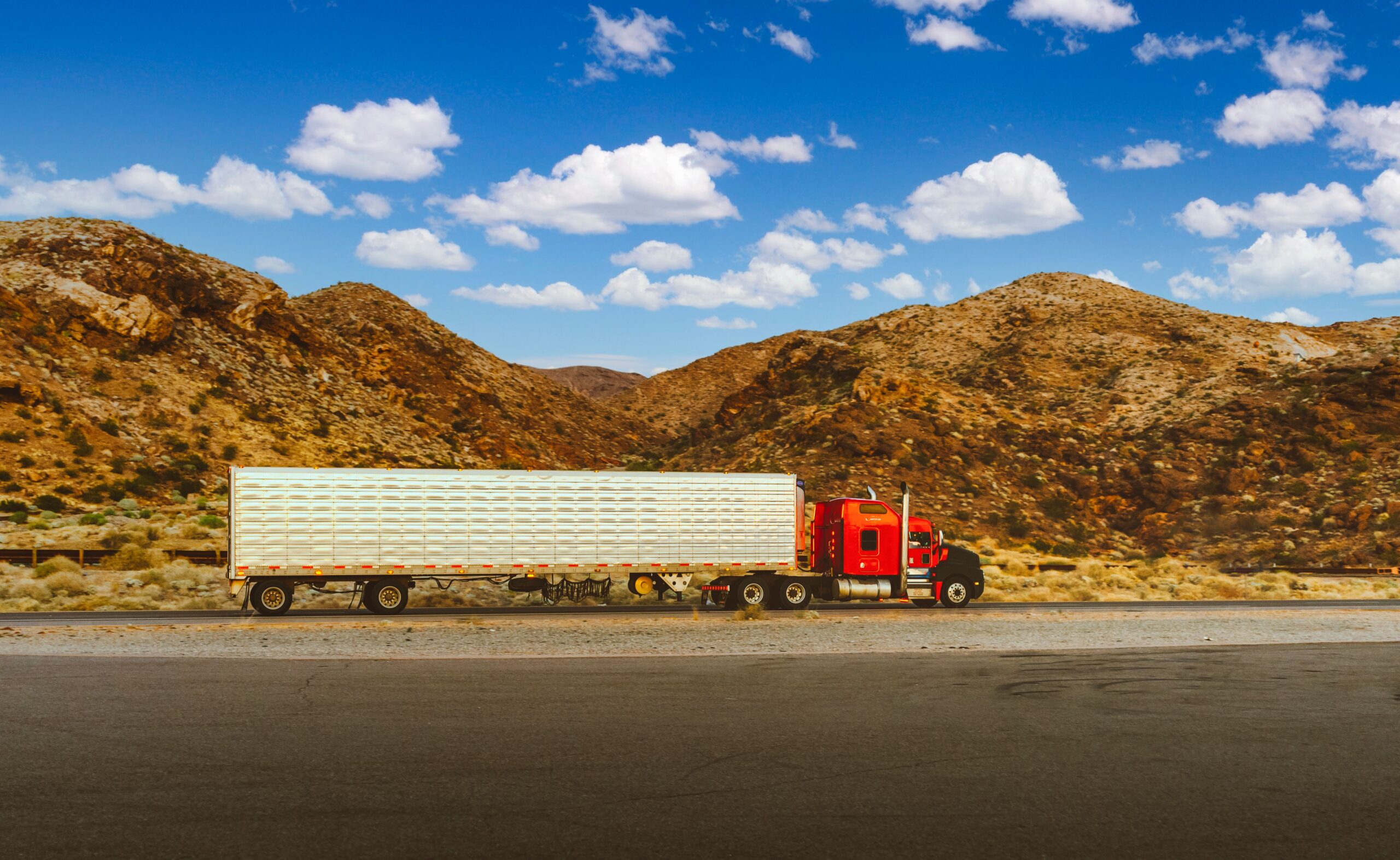 project-2 A vibrant red semi-truck travels through a desert highway with mountain views in Nevada.